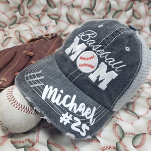 May include: A grey baseball cap with a white mesh back. The cap has the text "Baseball Mom" embroidered on the front in white with a white baseball graphic. The text "Michael #25" is embroidered on the brim in white.