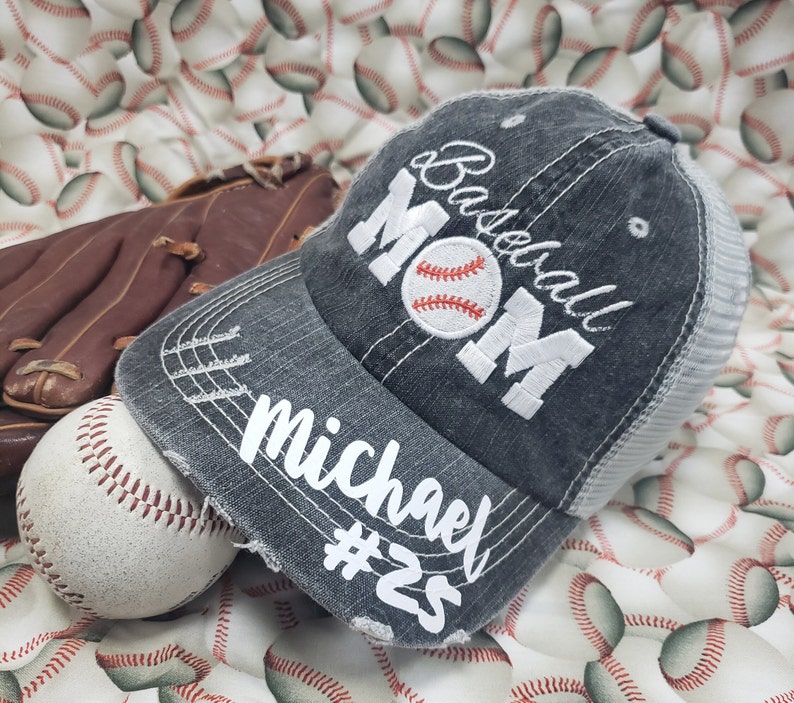 May include: A grey baseball cap with a white mesh back. The cap has the text "Baseball Mom" embroidered on the front in white with a white baseball graphic. The text "Michael #25" is embroidered on the brim in white.