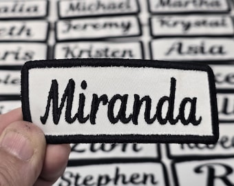 May include: White fabric patch with a black embroidered border and the name "Miranda" in black cursive lettering.