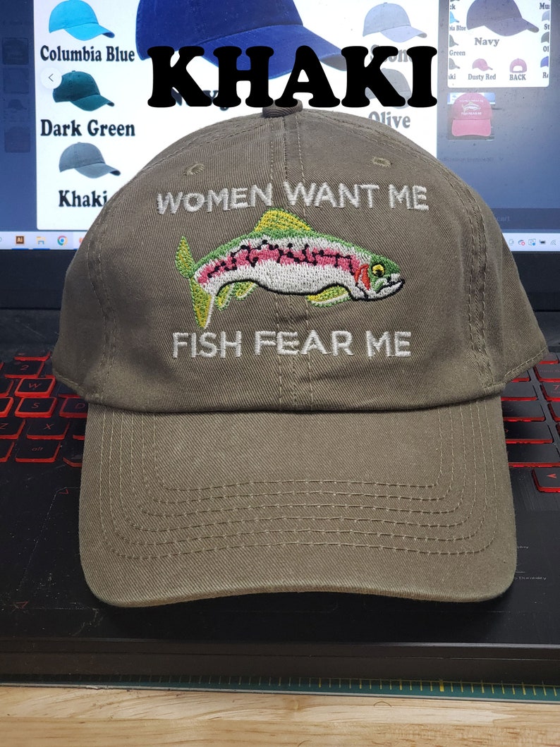 May include: Khaki baseball cap with an embroidered trout and the text "Women Want Me Fish Fear Me".