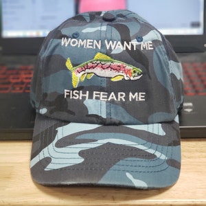 May include: A blue camouflage baseball cap with the text "Women Want Me" and "Fish Fear Me" embroidered on the front. A colorful fish is embroidered between the text.