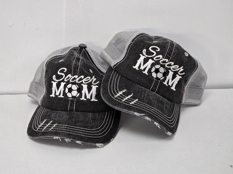 May include: Two black and gray trucker hats with white embroidered text that says "Soccer Mom" and a soccer ball graphic.