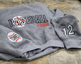 May include: Gray sweatshirt with baseball-themed embroidery. The word "BASEBALL" is across the chest, with a baseball graphic. The word "Mama" is embroidered in red. One sleeve has the number "12" and the other has a baseball patch with the name "Torres".