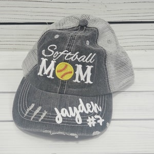 May include: A distressed trucker hat in grey and white with the text "Softball Mom" and a yellow softball with red stitching. The hat also has the name "Jayden" and the number "#7" embroidered on the front.