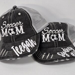 May include: Two black and gray mesh trucker hats with the text "Soccer Mom" embroidered on the front. The hats have a white soccer ball graphic and are personalized with the names "Teegan" and "Sydney".