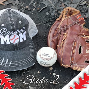 May include: A grey and white baseball cap with the text "Baseball Mom" and a baseball graphic. A brown leather baseball mitt and a white baseball are on a dark brown surface. The text "Style 2" is written at the bottom of the image.