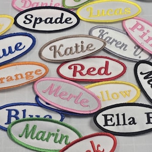 May include: A collection of colorful embroidered iron-on patches with names like "Blue", "Orange", "Red", "Marin", "Ella B", "Katie", "Karen U.", "Spade", "Lucas", and "Pink".