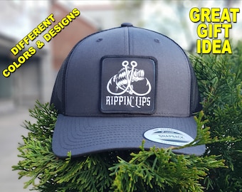 May include: A black and gray trucker hat with a black patch that says "Rippin' Lips" and a white graphic of a fish with two hooks. The hat has a black mesh back and a gray front.