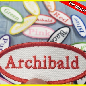 May include: Oval-shaped embroidered patches with various colors and names. One patch reads "Archibald" in red thread. Other patches display colors like green, yellow, and pink. The patches are on a denim background, with a "Top Quality Patch" banner.
