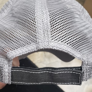 May include: Gray and black mesh trucker hat with a black adjustable strap in the back.