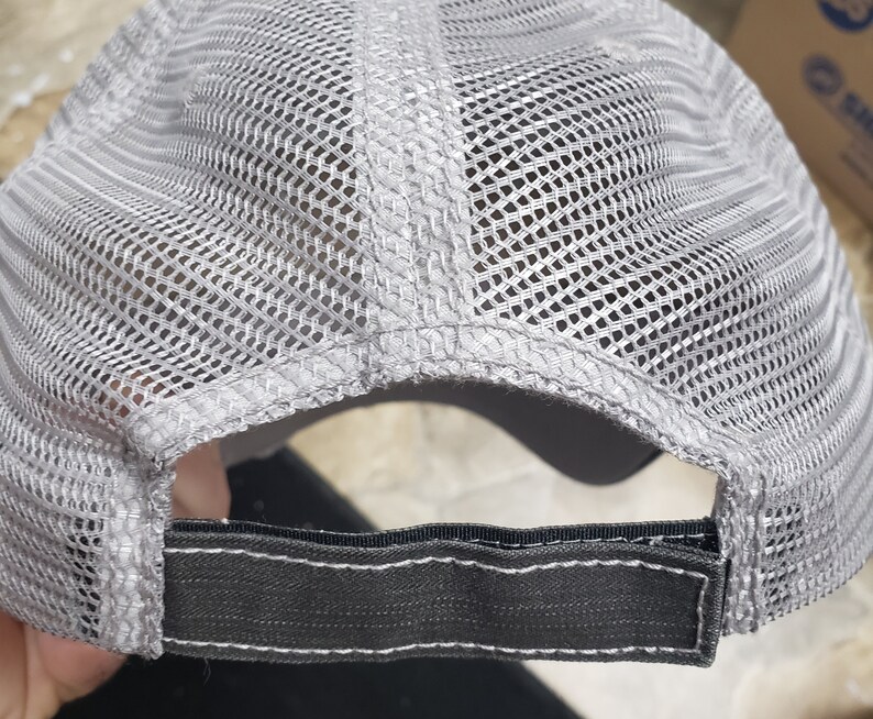 May include: Gray and black mesh trucker hat with a black adjustable strap in the back.