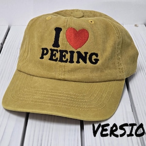 May include: A khaki baseball cap with black embroidery that reads "I ♥ PEEING" with a red heart.