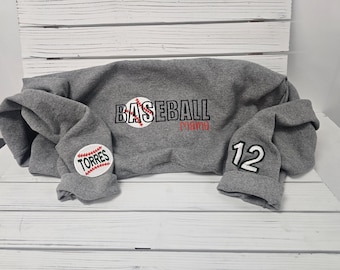 May include: Gray sweatshirt with the text "BASEBALL Mama" and a baseball graphic on the front. The left sleeve has a baseball graphic with the text "TORRES" and the right sleeve has the number "12" on it.