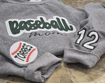 May include: Gray sweatshirt with a green and white baseball graphic, a red and white baseball patch, and a white number 12 patch. The text on the sweatshirt reads "Baseball Mom".
