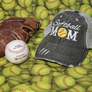 May include: A grey and black baseball cap with the text "Softball Mom" embroidered on the front. A yellow softball with white stitching is embroidered inside the word "Mom". The cap is surrounded by yellow baseballs.