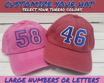 May include: Two baseball caps with large embroidered numbers. One cap is pink with blue and pink numbers "58". The other cap is red with blue numbers "46". The text "Customize Your Hat Select Your Thread Colors" is at the top of the image. The text "Large Numbers or Letters" is at the bottom of the image.