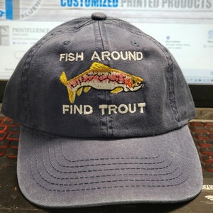 May include: Navy blue baseball cap with the embroidered text "FISH AROUND FIND TROUT" and a colorful fish graphic. The hat has a curved brim and a button on top. A perfect accessory for fishing enthusiasts.