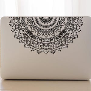 May include: A white laptop with a black mandala design sticker on the lid. The mandala is a circular design with intricate details.