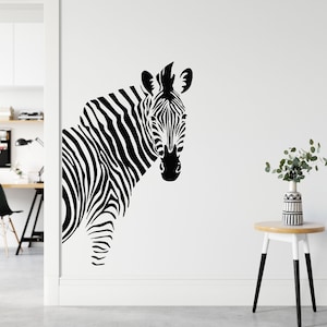 Op de afbeelding: Zwart-witte zebrakop silhouet wand sticker. De zebra kijkt naar de kijker met zijn hoofd lichtjes naar de zijkant gekanteld. De sticker is op een witte muur.