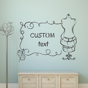 May include: Black and white wall decal featuring a tailor's dress form with measuring tapes, a spool of thread, and the words "CUSTOM text" inside a decorative frame. The design is suitable for a sewing room or craft space.