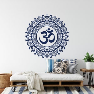 May include: A navy blue Om symbol mandala wall decal with intricate details. The decal is displayed on a white wall above a white couch with pillows and a throw blanket.