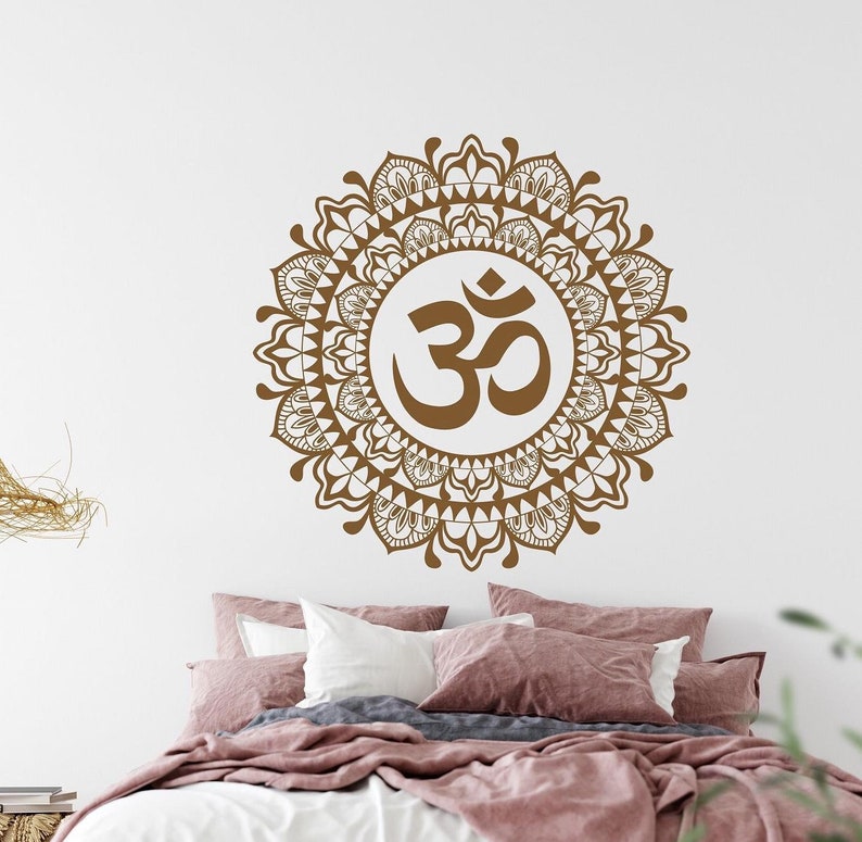 May include: A brown Om symbol surrounded by a detailed mandala design. The mandala is a circular pattern with intricate details and floral motifs. The design is on a white background.