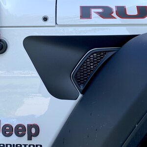May include: White Jeep Gladiator with black fender flares and a black and red "RUBICON" decal on the side. The Jeep has a black antenna and a black and red "Jeep" logo on the side.