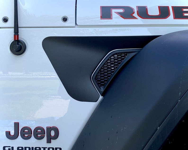 May include: White Jeep Gladiator with black fender flares and a black and red "RUBICON" decal on the side. The Jeep has a black antenna and a black and red "Jeep" logo on the side.