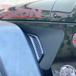 May include: A black Jeep Wrangler Rubicon with red accents. The vehicle has a Trail Rated badge and a Jeep logo on the fender.