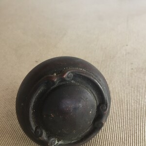 May include: A dark brown, round, decorative knob with a raised, ornate design. The knob has a smooth, slightly textured surface.