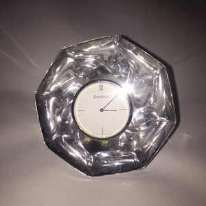 May include: A clear glass clock with a silver face and hands. The clock face reads "Orrefors" and "Swiss Movement".