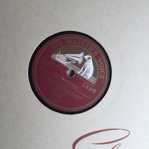 Op de afbeelding: Een rode vinylplaat met een zwart label. Het label toont een cartoonhond die naar een grammofoon luistert. De tekst "His Master's Voice" is gedrukt in een gouden cirkel rond de hond. De tekst "Made in England E.H. 619" is gedrukt op het label. De tekst "Zwei Marchenaugen" is gedrukt op het label. De tekst "Lied und Fox-Trot aus "Die Zirkusprinzessin" (Kalman)" is gedrukt op het label. De tekst "Marcel Wittrisch mit Orchester Dirigent: Clemens Schmalstich" is gedrukt op het label. De tekst "Blem 62-776" is gedrukt op het label.