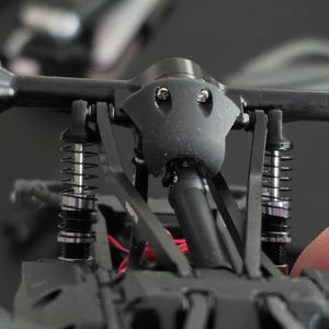May include: Close-up of a black RC car chassis, showcasing the suspension system. The image highlights the shock absorbers, springs, and structural components, with a focus on the vehicle's mechanical details.