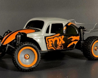 May include: A white and orange remote control car with a black "FOX" logo on the side. The car has a clear plastic spoiler and black wheels with orange rims.
