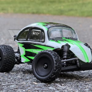 May include: A green and white toy car with black accents and a black windshield. The car has a rounded body and large wheels.