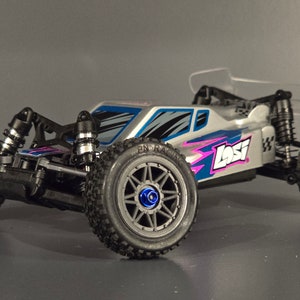 Peut inclure: Une voiture télécommandée argentée et bleue avec un aileron arrière transparent. La voiture a des pneus noirs et un design rose et bleu sur le côté. La voiture a le mot "Losi" imprimé sur le côté.