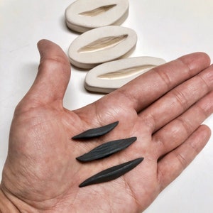 May include: Three black ceramic leaf-shaped pieces, similar to the shape of the three white ceramic molds in the background.