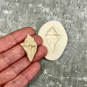 Op de afbeelding: Een witte schelpvorm en een witte schelp gemaakt van de vorm. De vorm is ovaal en de schelp is een gedetailleerde replica van een schelp.