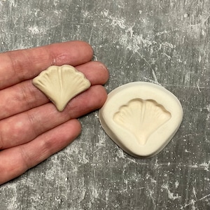 Può includere: Uno stampo in ceramica bianca e una fusione in ceramica bianca di una foglia di ginkgo.