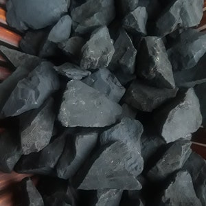 May include: A close-up of a pile of black, rough-hewn stones. The stones are various sizes and shapes, and they are all very dark in color.