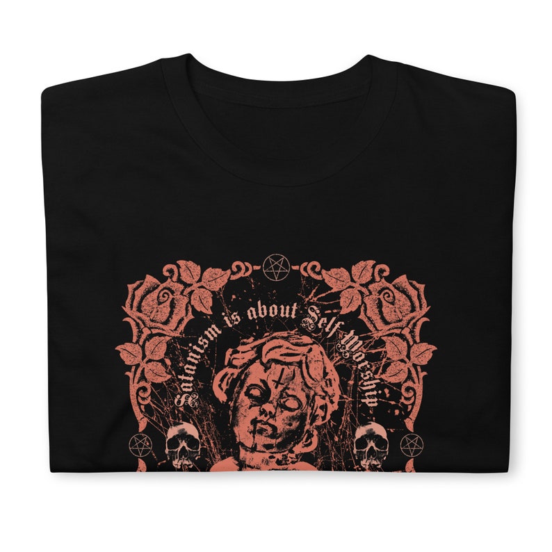 May include: Black t-shirt with a pink graphic design featuring a stylized image of a person's head with a pentagram on the forehead. The graphic also includes roses, skulls, and the text "Satanism is about Self Worship".