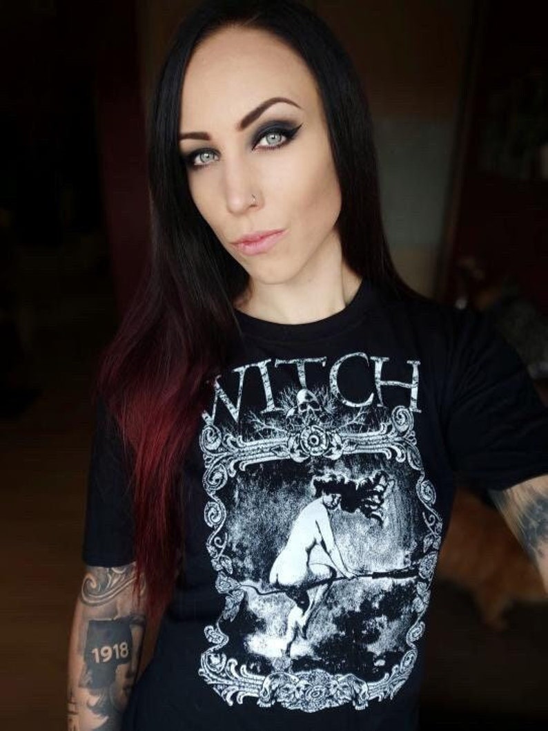 Peut inclure: T-shirt noir avec un motif blanc d'une femme chevauchant un balai. Le motif est encadr&eacute; d'une bordure d&eacute;corative et le mot "WITCH" est imprim&eacute; au-dessus du motif.