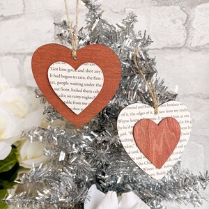 Peut inclure: Deux décorations en forme de cœur en bois avec un fond de page de livre. La décoration du haut est rouge et comporte le texte "Got him good and shot any. It had begun to rain, the first t. keet, people waiting under the out front, hailed them caba. ked it on rainy nights. vable from me. shot to". La décoration du bas est brune et comporte le texte "esmond and Feilheir brothers wc. of it, the edges of it. new from my readin. Wayne knewmore. I store him at one. hy he'd ne. of it. He g. said, "B. vent ho. ething. Uncle. aken. gain. ed took. and g. he said wa. t as the. the Cha. ob, run. Winter before. were Buddy"