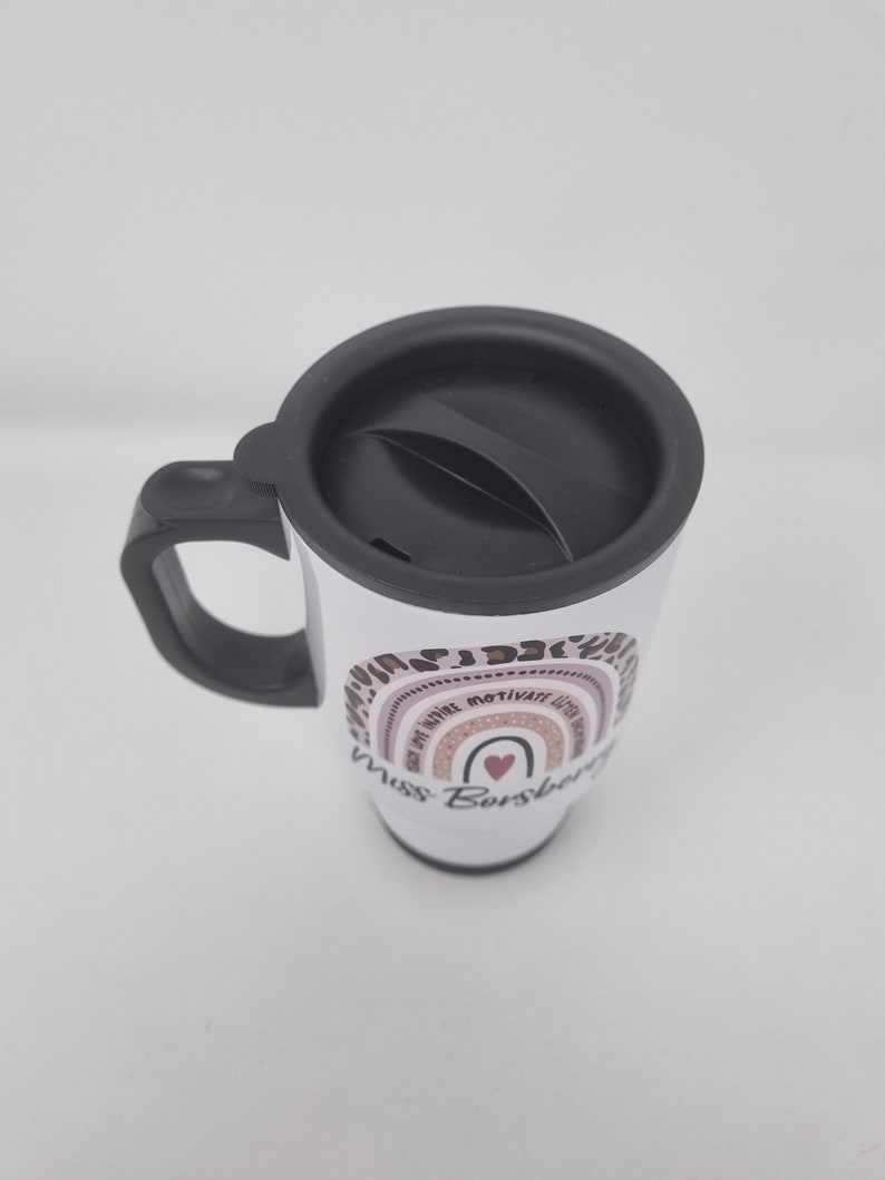 May include: White travel mug with a black lid and handle. The mug has a rainbow design with the words "Be Kind, Be Brave, Be Motivated, Be You" and "Miss Borsberg" printed on it.