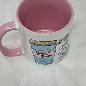 May include: White ceramic coffee mug with a pink handle and a blue and gold illustration of a coffee cup with the text "Boss Babe". The mug has a pink interior and the text "Ingredients for the perfect F*CK IT" on the side.