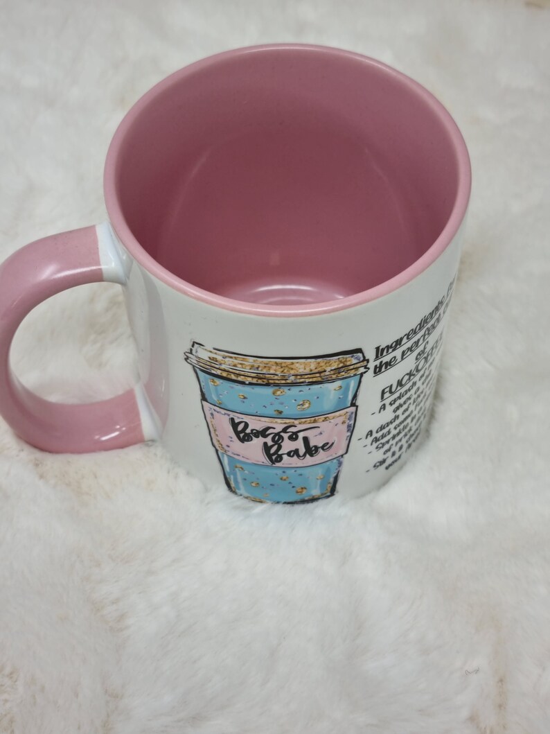 May include: White ceramic coffee mug with a pink handle and a blue and gold illustration of a coffee cup with the text "Boss Babe". The mug has a pink interior and the text "Ingredients for the perfect F*CK IT" on the side.