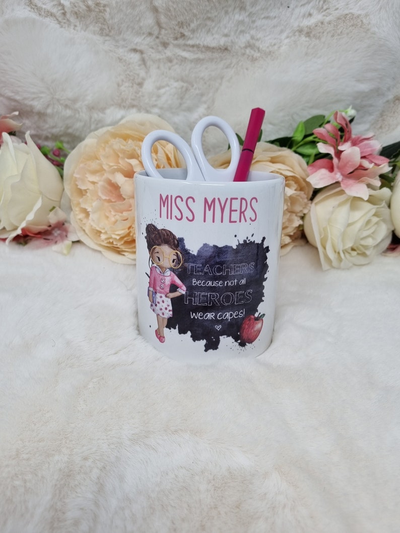 May include: White ceramic pencil holder with a black and white illustration of a teacher with the text "Miss Myers" and "Teachers because not all heroes wear capes!"
