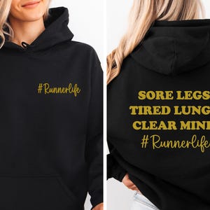 May include: Black hoodie with gold text. The front of the hoodie says "#Runnerlife". The back of the hoodie says "Sore legs. Tired lungs. Clear mind. #Runnerlife".