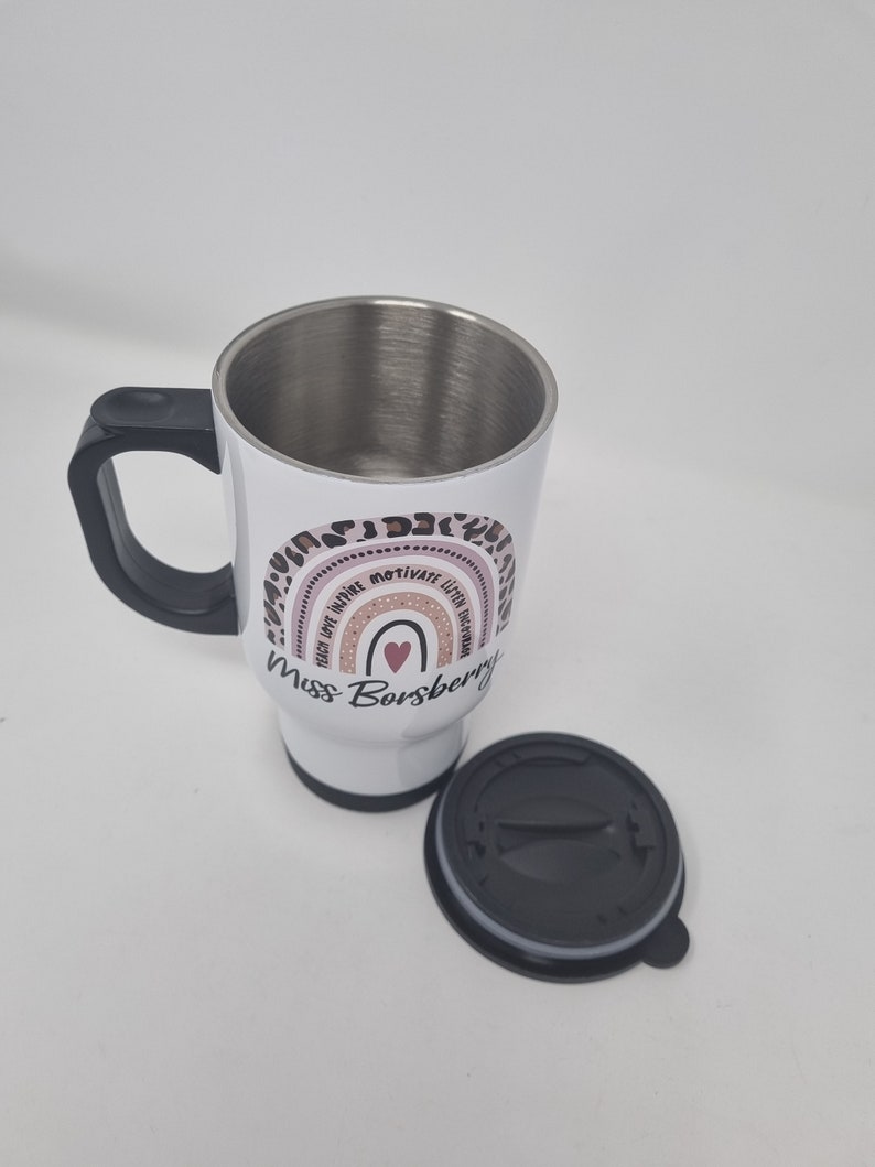 May include: White stainless steel travel mug with a black handle and lid. The mug has a pink and brown rainbow design with the text "Teach Love Inspire Motivate  Little Humans" and "Miss Borsberry".