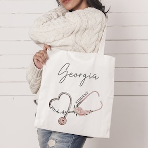 May include: White canvas tote bag with the name "Georgia" written in black cursive. The bag features a pink floral design with a stethoscope and the words "Midwife Student".
